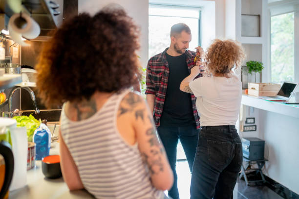 Young curly haired woman putting beer bottle into flatmate's shirt pocket Young blond curly haired woman in the kitchen with friends putting beer bottle into her male flatmate's shirt pocket for fun flatmate stock pictures, royalty-free photos & images