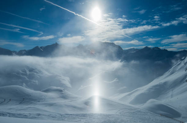 Panoramic view down snow covered valley in alpine mountain range with frost and sunlight sundog in air over ski piste