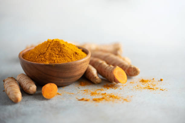 Turmeric powder in wooden bowl and fresh turmeric root on grey concrete background. Banner with copy space stock photo