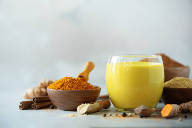 Hot healthy drink. Turmeric latte, golden milk with turmeric root, ginger powder, black pepper over grey background. Copy space. Spices for ayurvedic treatment. Alternative medicine concept. stock photo
