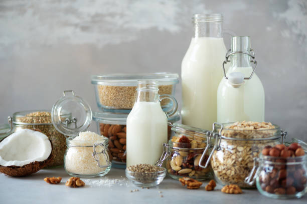 Glass bottles of vegan plant milk and almonds, nuts, coconut, hemp seed milk on grey concrete background. Banner with copy space. Dairy free milk substitute drinks and ingredients stock photo