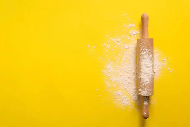 Rolling pin with flour on yellow background. Baking, menu, recipe concept. Top view. Banner with copy space for your text.