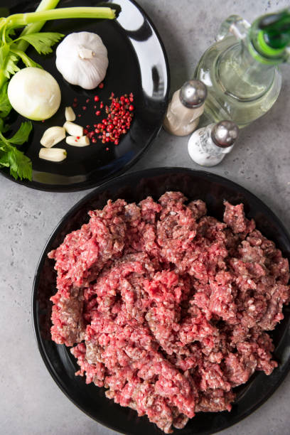 istock raw ground beef on a black plate, onions, garlic, celery, pepper on a plate, salt shaker, a bottle of sunflower oil, meat 1149547148