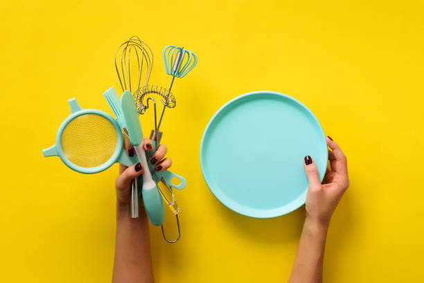 istock Woman hand holding kitchen utensils on yellow background. Baking tools - plate, brush, whisk, spatula. Bakery, cooking, healthy homemade food concept. Copy space 1149547181