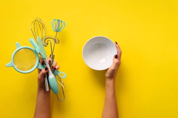 istock Woman hand holding kitchen utensils on yellow background. Baking tools - bowl, brush, whisk, spatula. Bakery, cooking, healthy homemade food concept. Copy space 1149547186