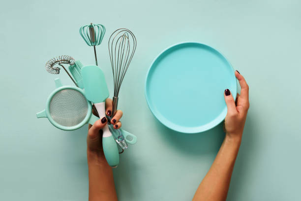 Woman hand holding kitchen utensils on pastel blue background. Baking tools - plate, brush, whisk, spatula. Bakery, cooking, healthy homemade food concept. Copy space