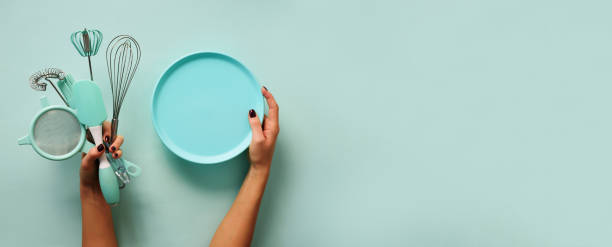 istock Baking flat lay. Female hands holding plate, kitchen tools, sieve, rolling pin, spatula and bruch on pastel blue background. Banner with copy space 1149547217