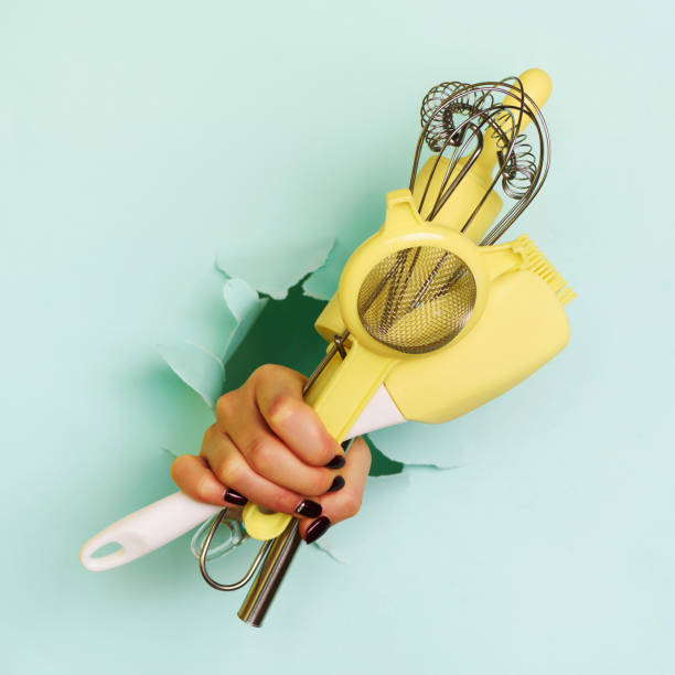 istock Woman hand holding kitchen utensils on blue background. Baking tools - brush, whisk, spatula. Bakery, cooking, healthy homemade food concept. Square crop 1149547258