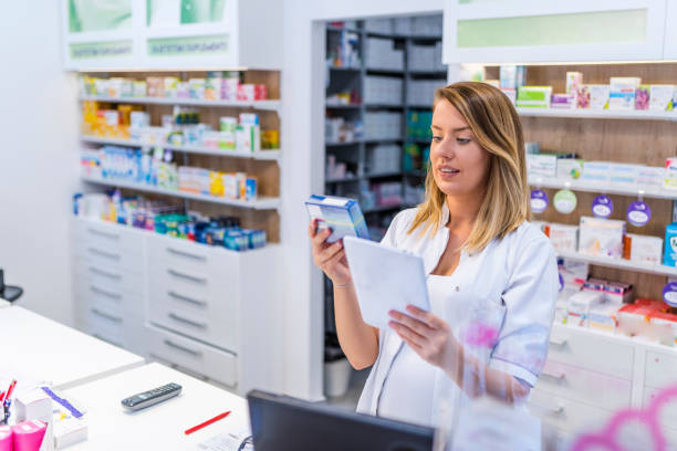 Young pharmacist holding a tablet and box of medications. Young pharmacist holding a tablet and box of medications. Young positive brunette pharmacist woman in drug store with tablet pc. Female pharmacist with digital tablet searching for medication pharmacy tech stock pictures, royalty-free photos & images