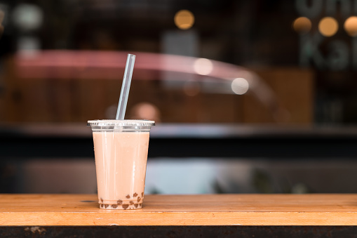 A disposable plastic cup with a straw containing bubble milk tea on a table in front of a cafe in Taipei.