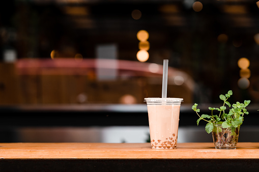 A disposable plastic cup with a straw containing bubble milk tea on a table in front of a cafe in Taipei.