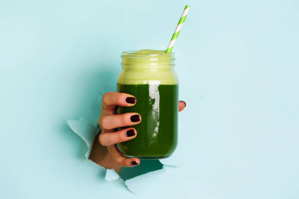 Woman hand holding glass jar of green smoothie, fresh juice against blue background. Healthy beverage, vegan, vegetarian concept. Banner with copy space stock photo