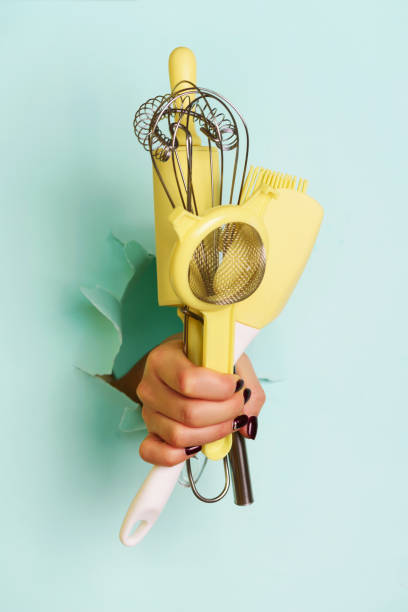 istock Woman hand holding kitchen utensils on blue background. Baking tools - brush, whisk, spatula. Bakery, cooking, healthy homemade food concept. Copy space 1149552893