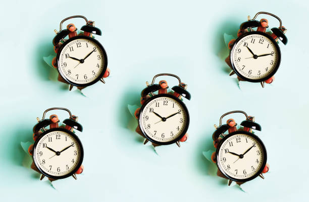 istock Chaotic pattern of hand holding black alarm clock through hole in blue paper background. Wake up alert concept. Morning routine. Banner with copy space 1149552988