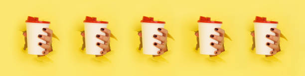 Pattern of female hand holding white paper mug on yellow background. Take away coffee cup concept. Mock up with copy space