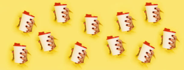 Chaotic pattern of female hand holding white paper mug on yellow background. Take away coffee cup concept. Mock up with copy space