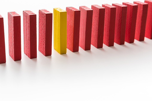 Uniqueness and individuality in crowd. One yellow wooden block between row of red ones, white background, free space