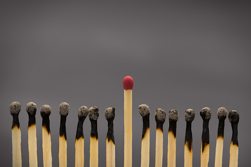 Power of mind. One unused matchstick among group of burnt matches on gray background, copy space