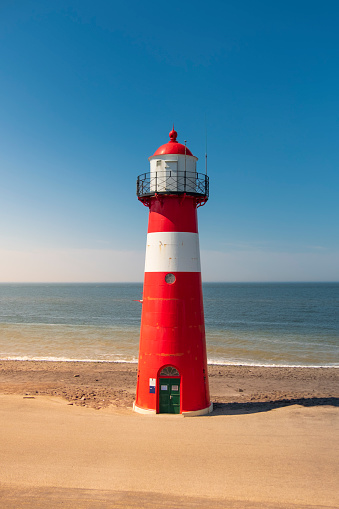 A red and white lighthouse at sea under a clear blue sky near Westkapelle in Zeeland, The Netherlands.