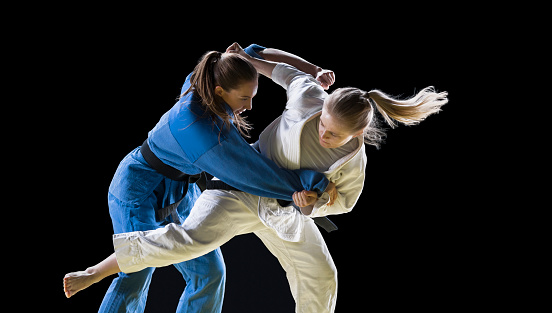 Female judo players fighting during the competition against black background.