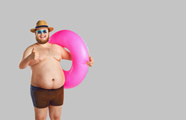 fat funny man in swimming trunks with an inflatable ring on a gray background. - summer people tourist slim imagens e fotografias de stock