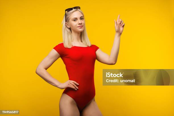 Pretty Blond Lifeguard In Red Swimsuit And Sunglasses Points Finger Up Stock Photo - Download Image Now