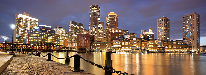 Downtown skyline city view of Boston Massachusetts USA looking over the riverfront harbor and marina boat dock from Fan Pier Park at night