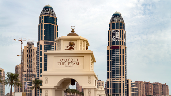 A typical example of urban landscaping in the modern Arabian city of Dubai, in the United Arab Emirates. In the background are skyscrapers of the area known as Jumeirah Lake Towers or JLT. In the foreground, date palms, flowering shrub and lawns. It is hard to believe that this is the Arabian desert; every blade of grass is artificially grown. In the background are also some villas by the roadside. Photo shot in the morning sunlight; horizontal format. Copy space. No people.