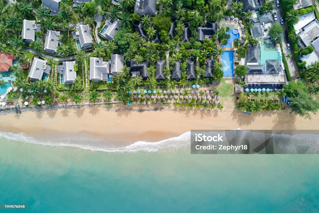 Aerial view of resort villa layout with coconut trees, umbrellas and deck chairs on the beach. Ocean wave reaching coastline. Beautiful tropical beach from top view. Andaman sea in Thailand. Summer holiday concept Beach Hut Stock Photo