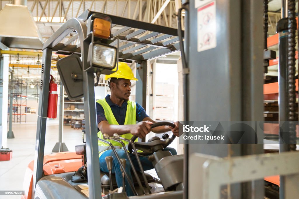 Male driver looking away while driving forklift Male driver looking away while driving forklift. Serious engineer is working in manufacturing company. He is in distribution warehouse. Forklift Stock Photo