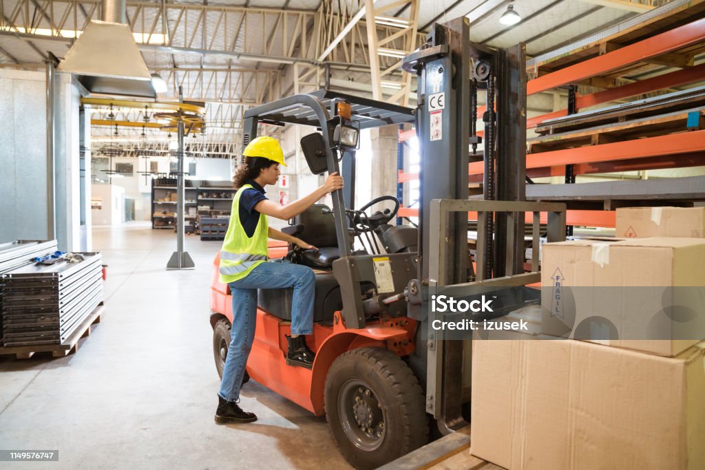 Full length of female driver boarding forklift Full length of female driver boarding forklift. She is wearing hardhat and reflective clothing in factory. Production worker is working in warehouse. Forklift Stock Photo