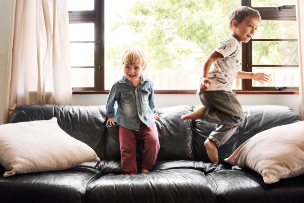 男の子達はいつもダメ - domestic life jumping child sofa ストックフォトと画像