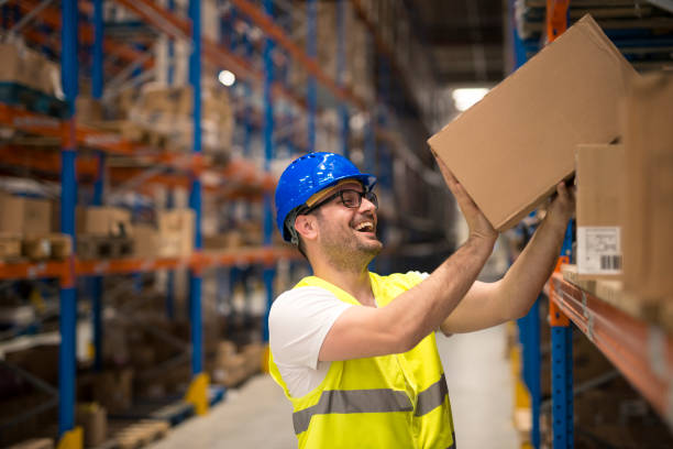 Working at warehouse. Smiling warehouse worker moving boxes on the shelf. Happy warehouse worker relocating boxes in storage compartment. big cardboard box stock pictures, royalty-free photos & images