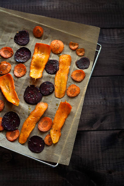 Preparing healthy beetroot and carrot chips on baking paper top view. Thin slices of vegetables seasoned with spices and olive oil