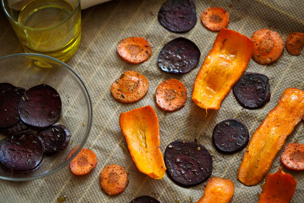 Preparing healthy beetroot and carrot chips with sea salt on baking paper close-up. Thin slices of vegetables seasoned with spices and olive oil