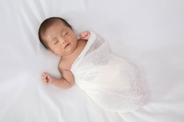 istock Sleeping newborn baby in white wrap while on white blanket background. 1149596888
