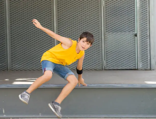 Front view of a smiling boy jumping over a metallic fence while looking camera on a bright day
