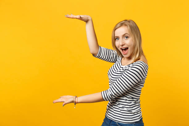 istock Excited funny young woman keeping mouth open, gesturing demonstrating size with vertical workspace isolated on yellow orange background. People sincere emotions, lifestyle concept. Mock up copy space. 1149608467