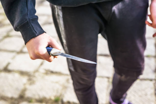 cerca de la mano de un joven con un cuchillo, una hoja grande. la arrogancia y la violencia entre los jóvenes. profundidad de enfoque poco profunda. - cuchillo arma fotografías e imágenes de stock