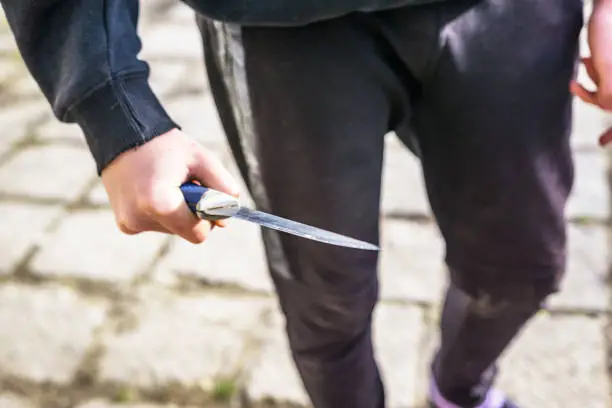 Close-up of a young man's hand with a knife, a big blade. Arrogance and violence among young people. Shallow depth of focus.