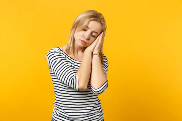 istock Relaxed young woman in striped clothes sleeping with folded hands under cheek isolated on yellow orange wall background in studio. People sincere emotions, lifestyle concept. Mock up copy space. 1149609641