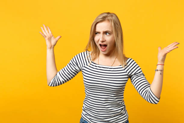 istock Irritated perplexed young woman in striped clothes looking aside, spreading hands, screaming isolated on yellow orange wall background. People sincere emotions, lifestyle concept. Mock up copy space. 1149610095