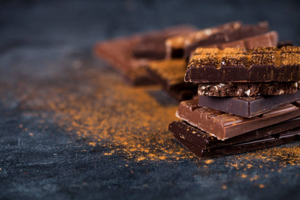 istock Broken chocolate stacked on black background. Chocolate bar pieces heap witn cinnamon powder. 1149612975