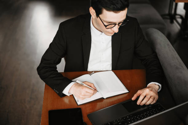 istock Upper view of a male hand writing in a notebook and operating on a laptop while sitting on a table. 1149616421