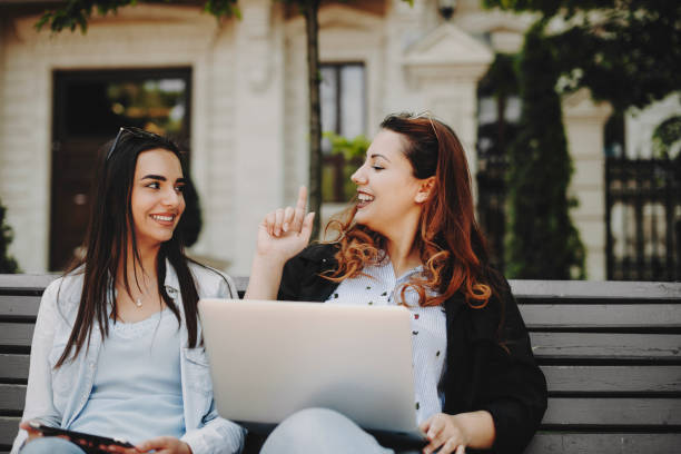 istock Cute plus size girl with red hair speaking with her girlfriend while showing something with a finger while another is looking smiling her against a building. 1149618261