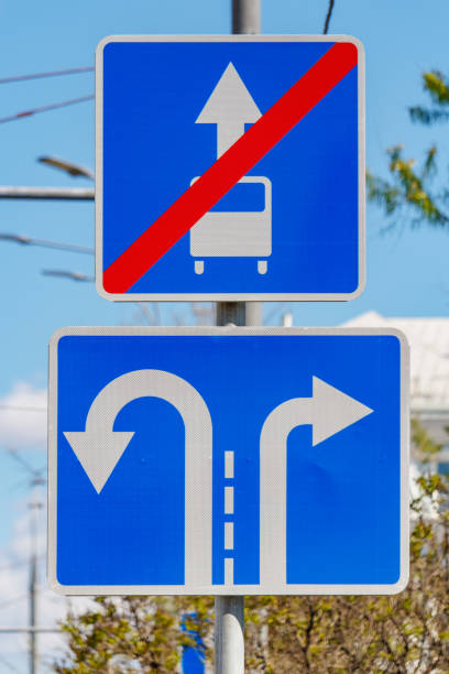 road signs direction of motion traffic on the lanes closeup against green trees and blue sky in sunny day - single line urban scene outdoors vertical imagens e fotografias de stock
