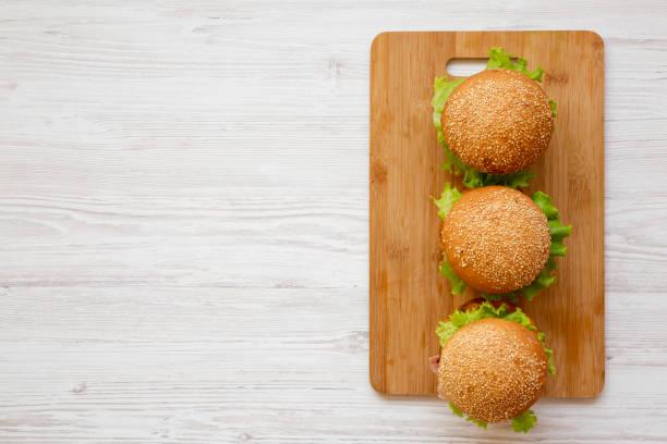 Homemade cheeseburgers on a bamboo board over white wooden background, overhead view. Flat lay, from above, top view. Copy space.