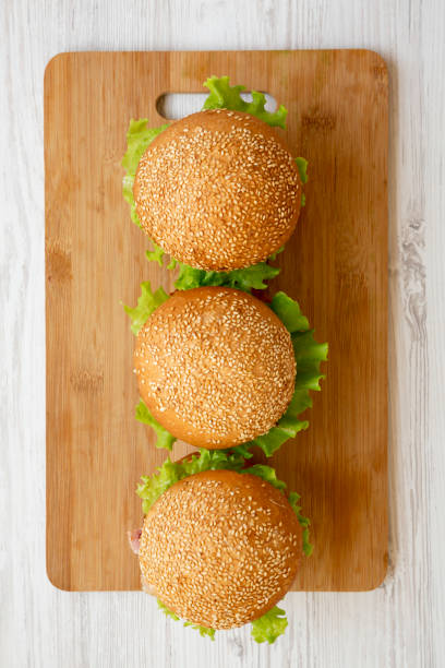 Homemade cheeseburgers on a bamboo board over white wooden surface, overhead view. Flat lay, from above. Close-up.