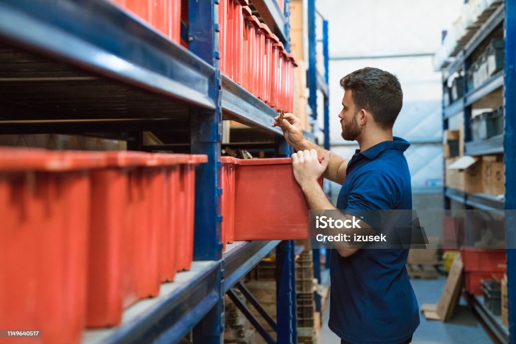 Warehouse male worker examining goods in factory Warehouse worker examining goods in factory. Young male laborer is working in shipping industry. He is standing by racks in warehouse. Warehouse Worker Stock Photo