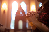 Woman hand holding rosary against cross and praying to God at church.